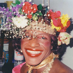 A woman smiling and wearing a hat covered in flowers.