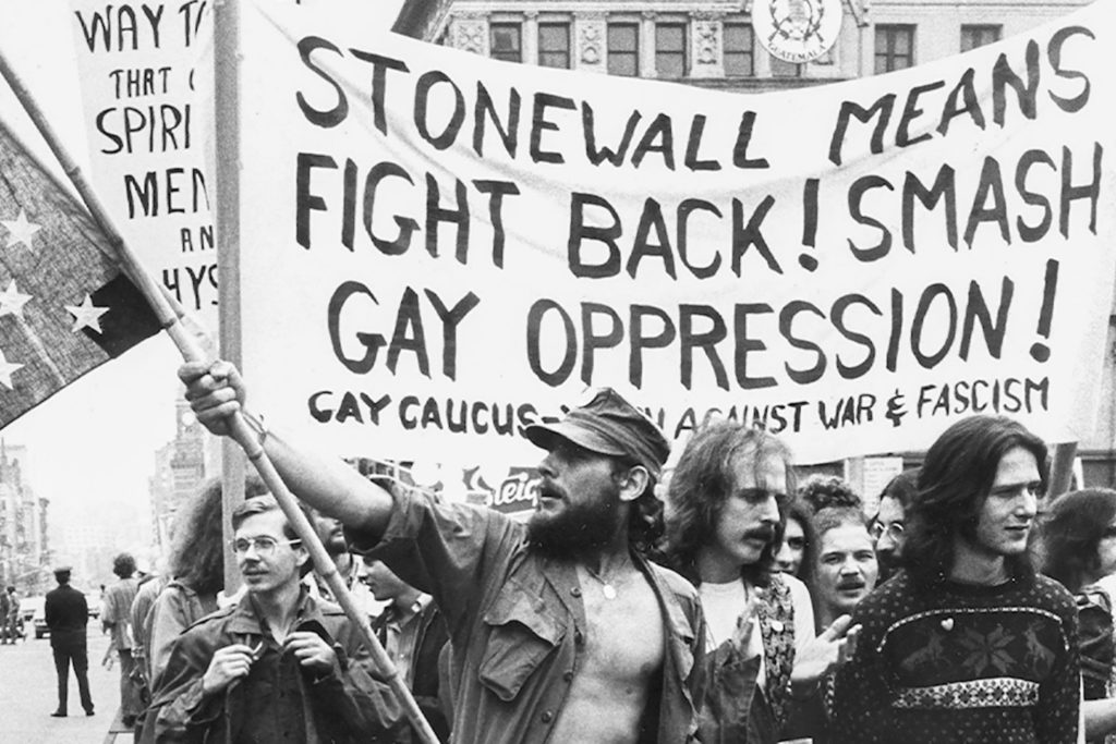 Protestors marching through the street holding signs during the Stonewall Riot.